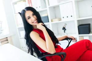 Beautiful young girl in a red suit is sitting in a chair in the office.