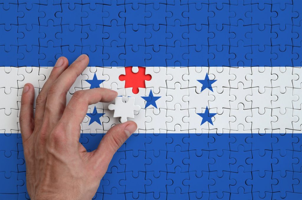 Honduras flag is depicted on a puzzle, which the man's hand completes to fold.